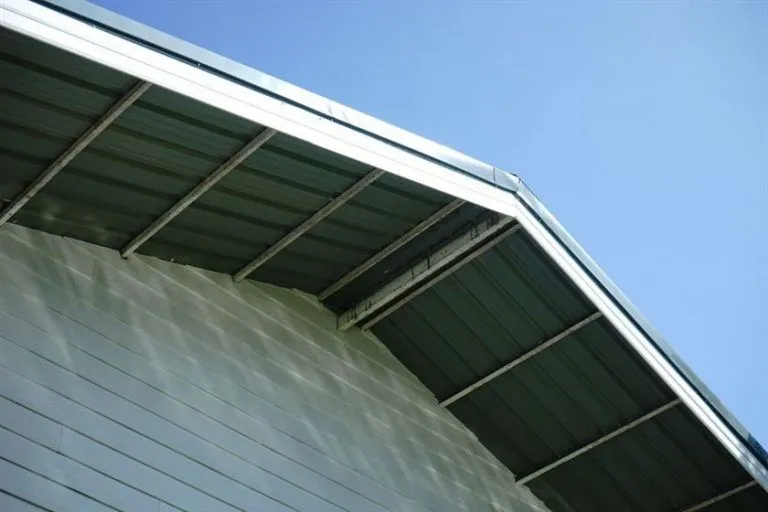 Close-up view of a house with a green sheet metal roof under a clear blue sky, highlighting its sleek and weather-resistant design