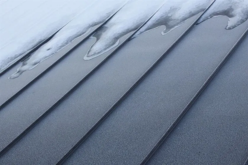 Close-up view of a zinc roof partially covered with snow, showcasing its sleek design and weather resistance